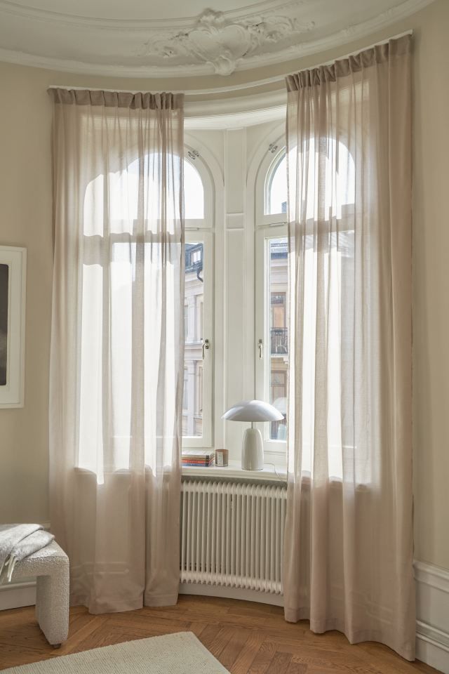 a living room with two windows and a radiator in the corner, along with a rug on the floor