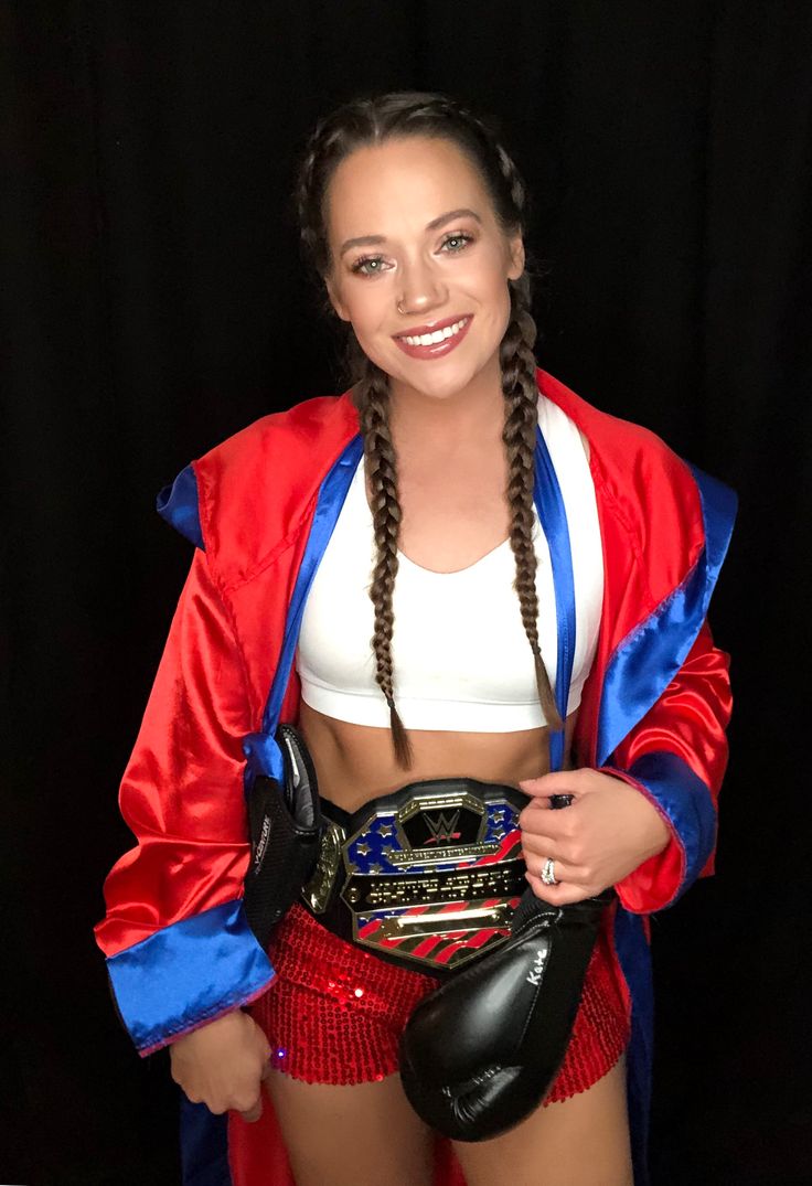 a woman in a red and blue outfit holding a wrestling belt with her hands on her hip