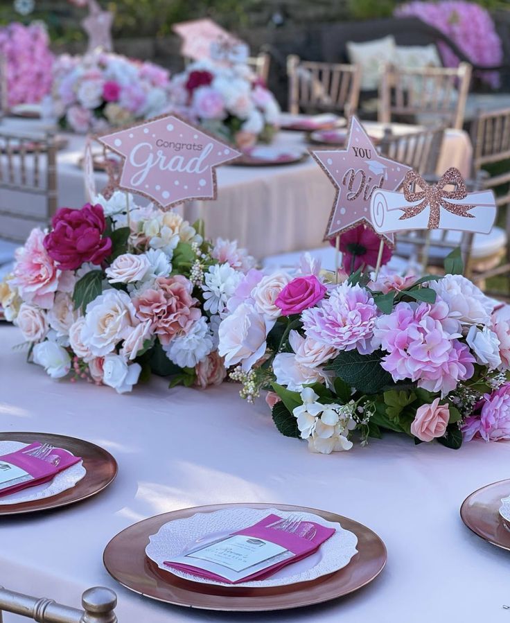 the table is set with pink and white flowers, gold place cards, and napkins