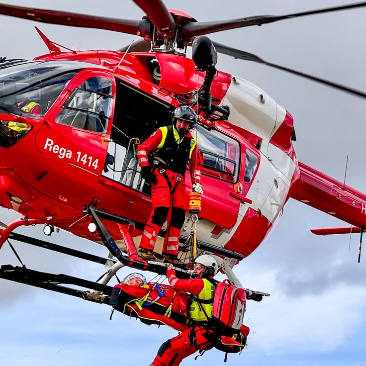 a red and white helicopter with two men on it's legs in the air