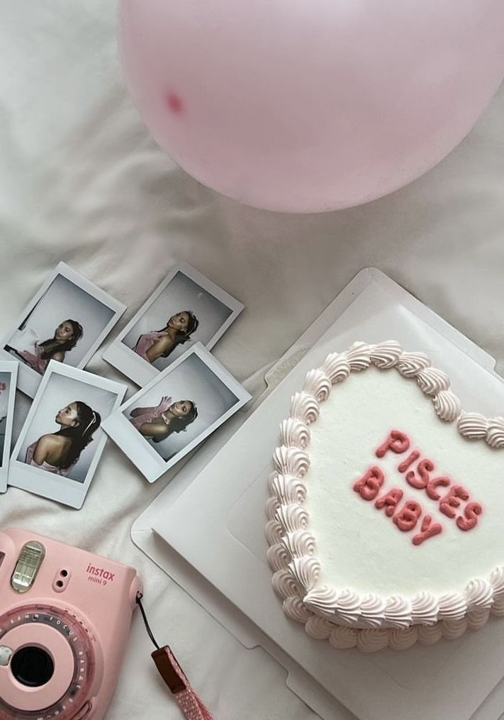 a birthday cake with pink frosting and pictures on it next to a camera, balloons, and other items