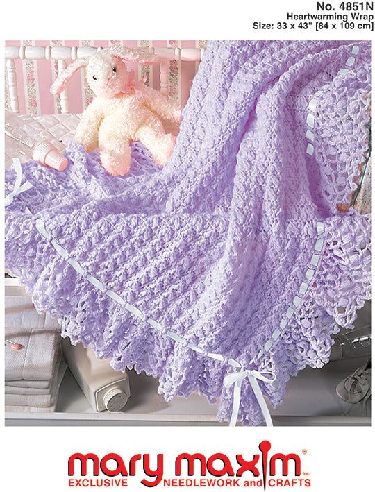 a crocheted baby blanket with a teddy bear sitting on the bed in it