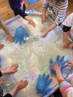 several children are playing in an ice tray with blue gloves on and hands reaching for something