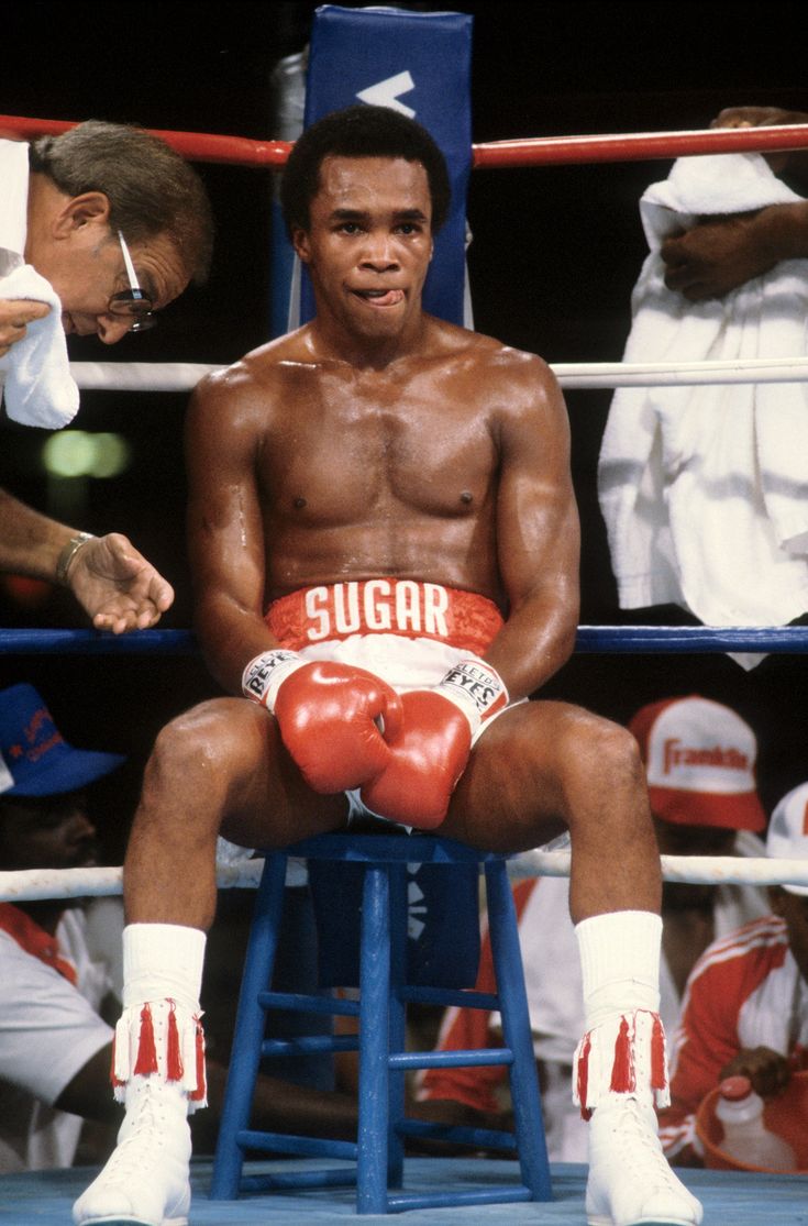 a man sitting on top of a blue chair in front of a crowd wearing boxing gloves