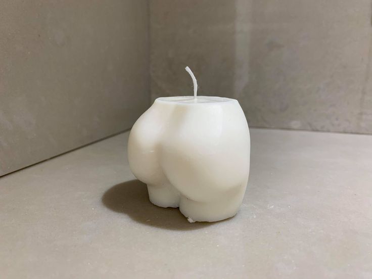 a white candle sitting on top of a table next to a gray tiled wall and floor