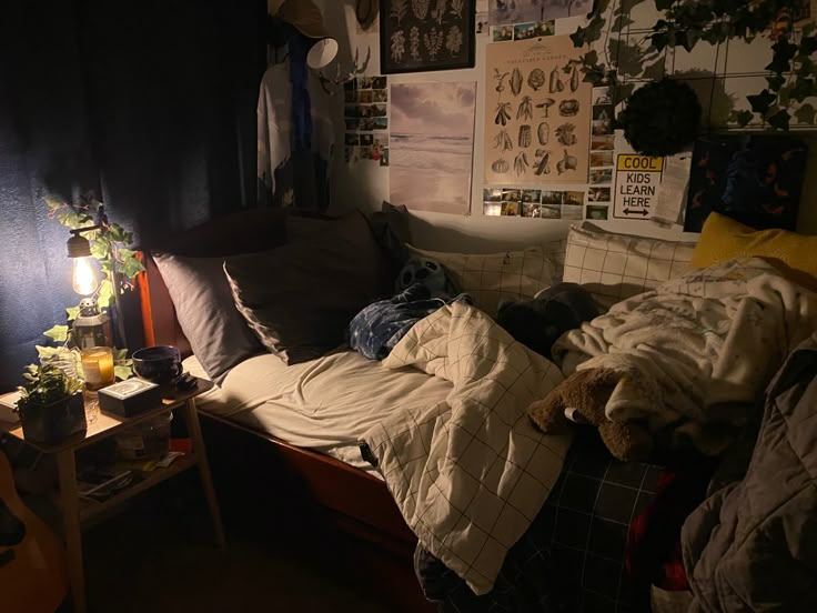 an unmade bed in a dark room with posters on the wall and a lamp next to it