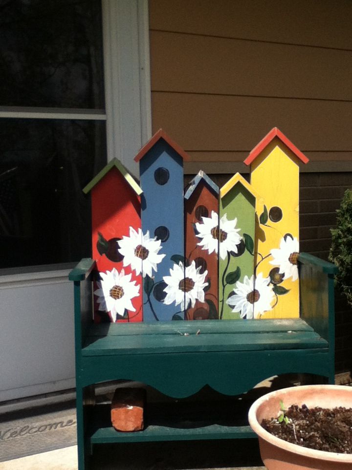 a potted plant sitting next to a bench with painted bird houses on it's back