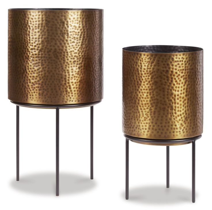 two metal planters sitting next to each other on top of black stand legs and one has a gold pattered finish