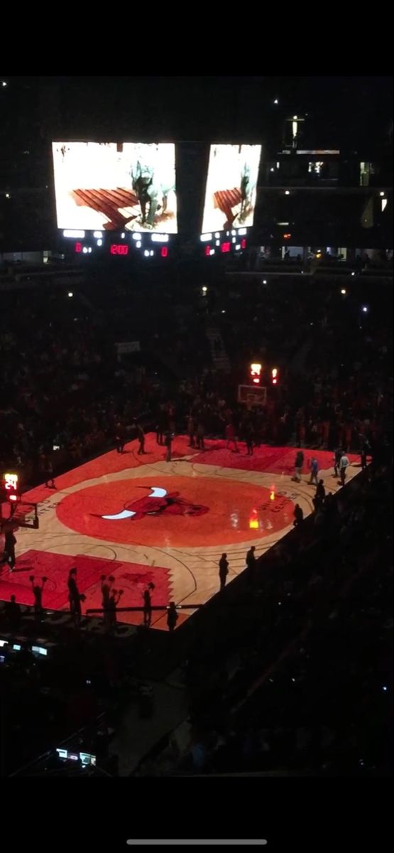 a basketball game is being played in an arena at night with large screens on the wall