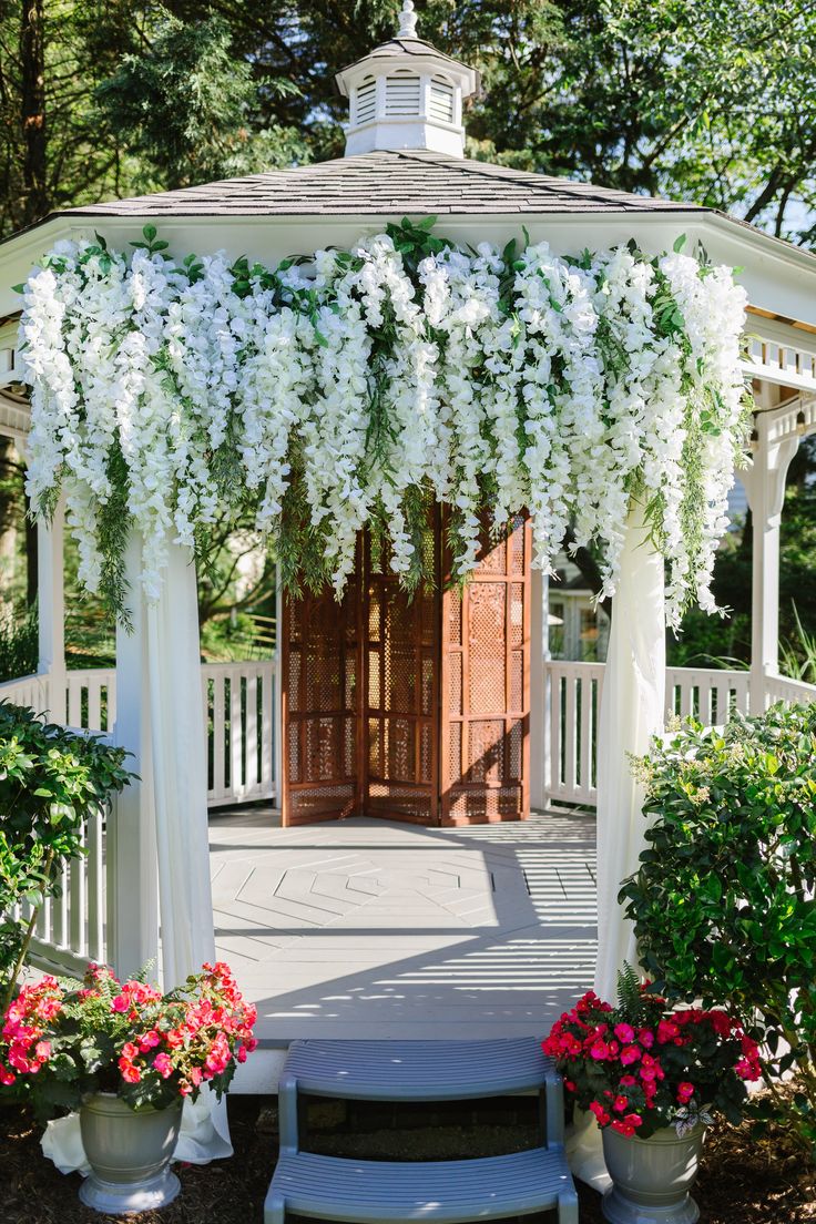 an outdoor gazebo with white flowers and greenery