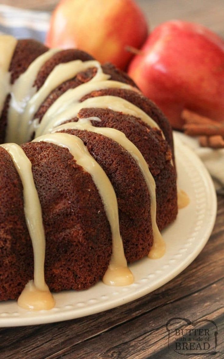 a bundt cake with icing on a plate next to apples and cinnamon sticks