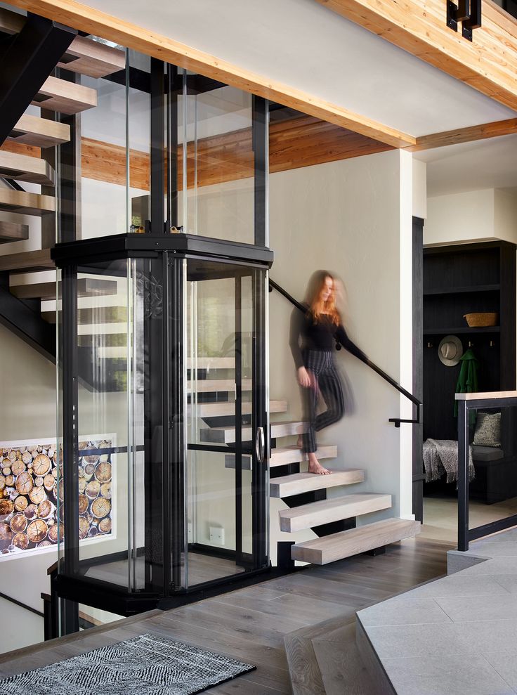 a woman is walking down the stairs in her home with glass walls and black railings