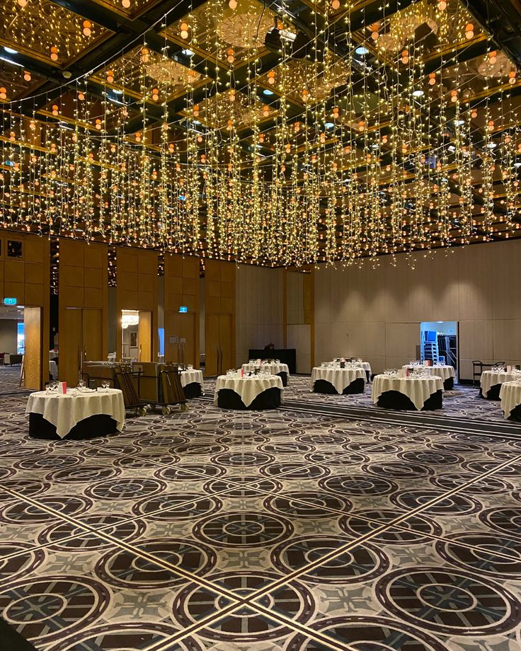 a banquet hall with tables and chairs covered in white tablecloths, chandeliers and lights hanging from the ceiling