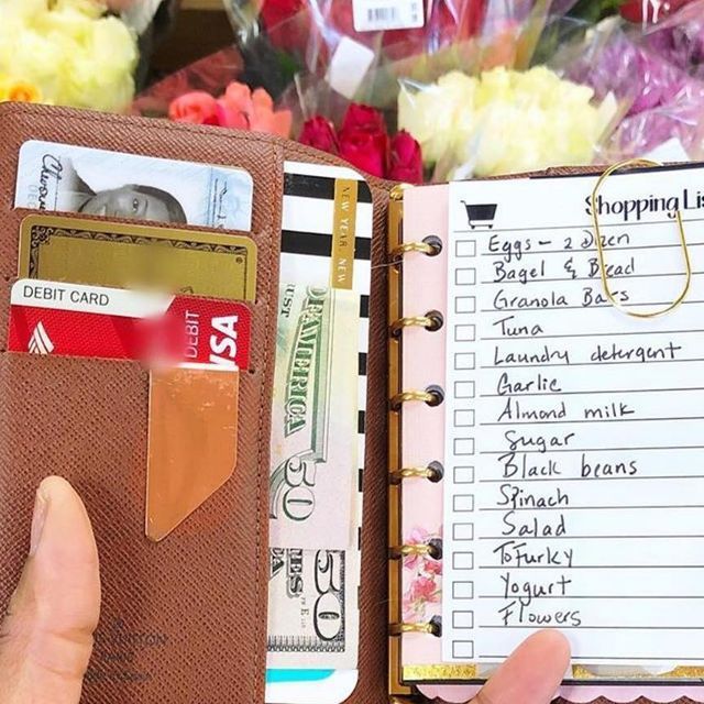 a person holding an open wallet in front of a bunch of flowers and writing on it