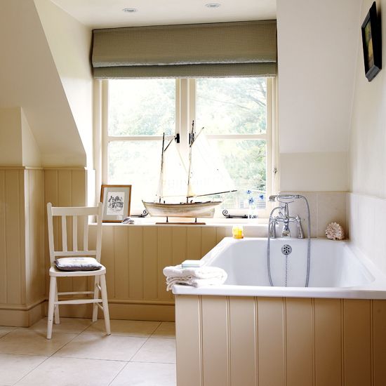 a bath tub sitting under a window next to a wooden rocking chair in a bathroom