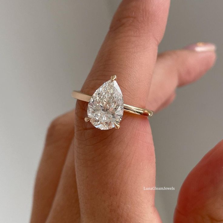 a woman's hand holding a ring with a pear shaped diamond