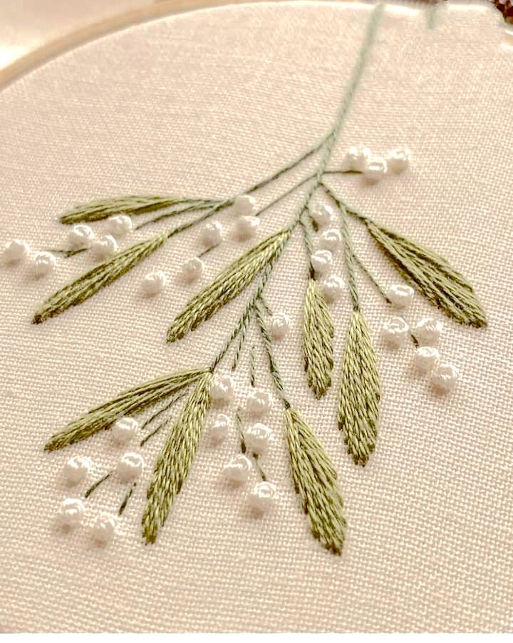 a close up of a embroidery on a hoop with white beads and green leaves in it