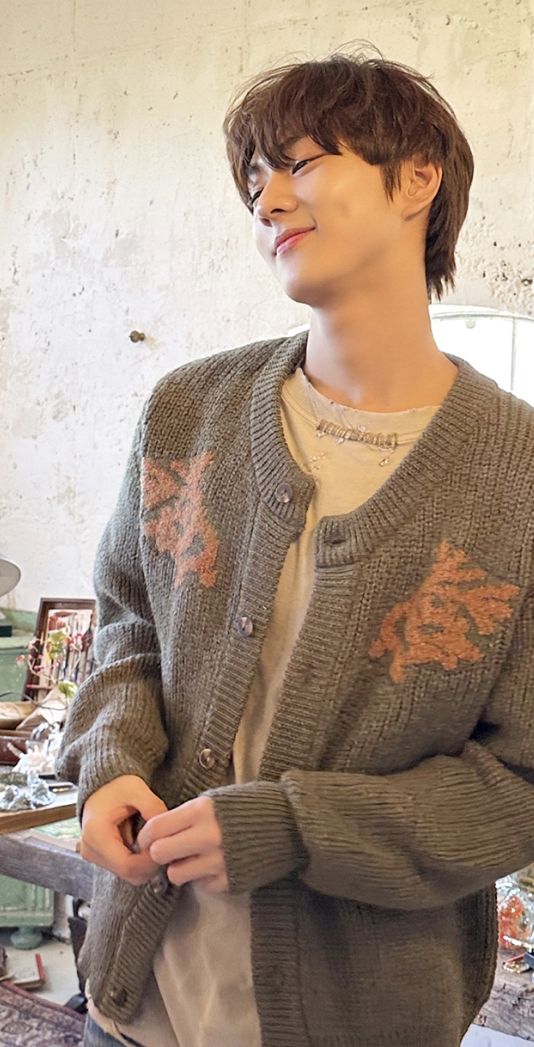 a young man standing in front of a table wearing a sweater and jeans, with his eyes closed