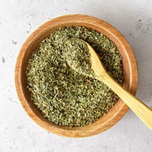 a wooden bowl filled with green herbs and a wooden spoon