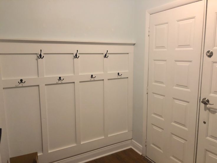 a room with several white doors and some hooks on the wall, along with a hard wood floor