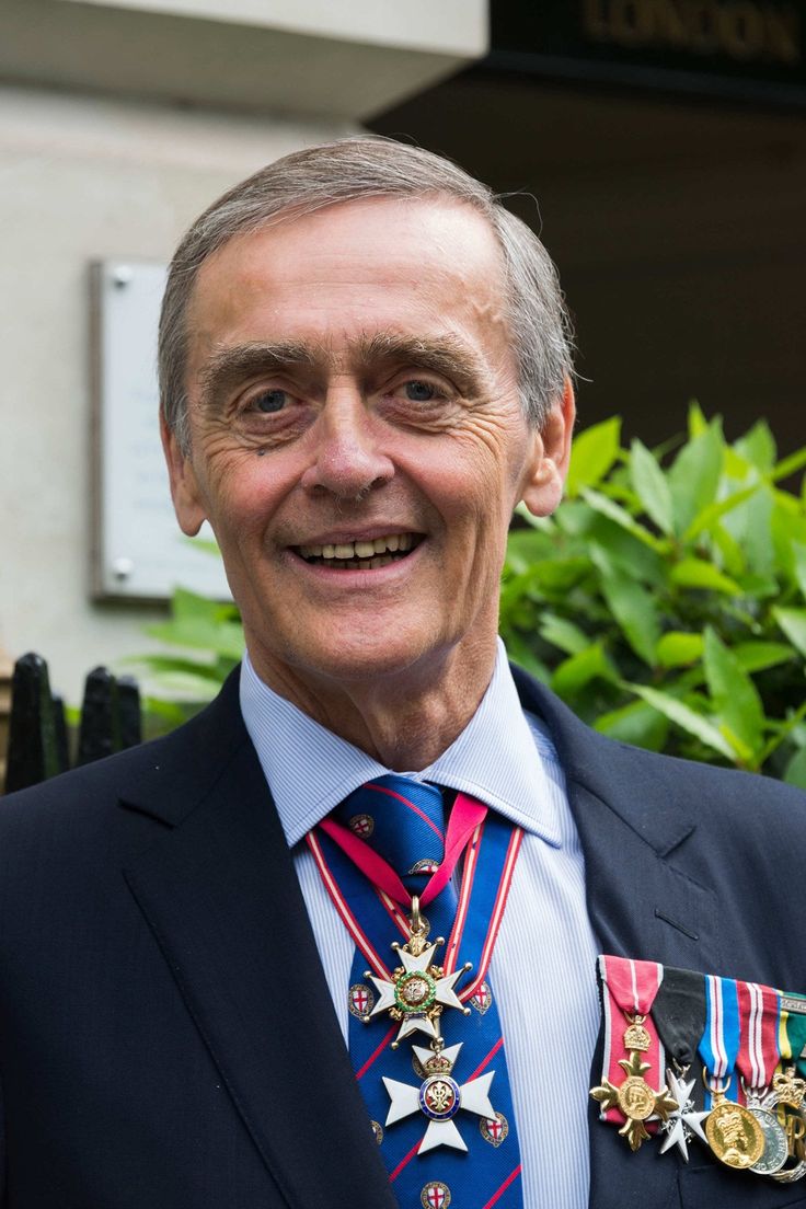 an older man in a suit with medals on his lapel smiling for the camera