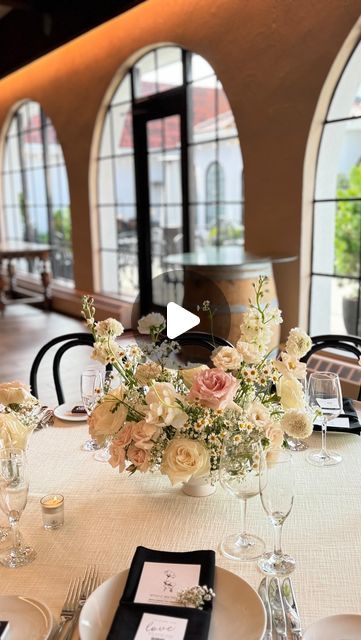 the table is set with flowers and place settings for an elegant wedding reception in front of large windows