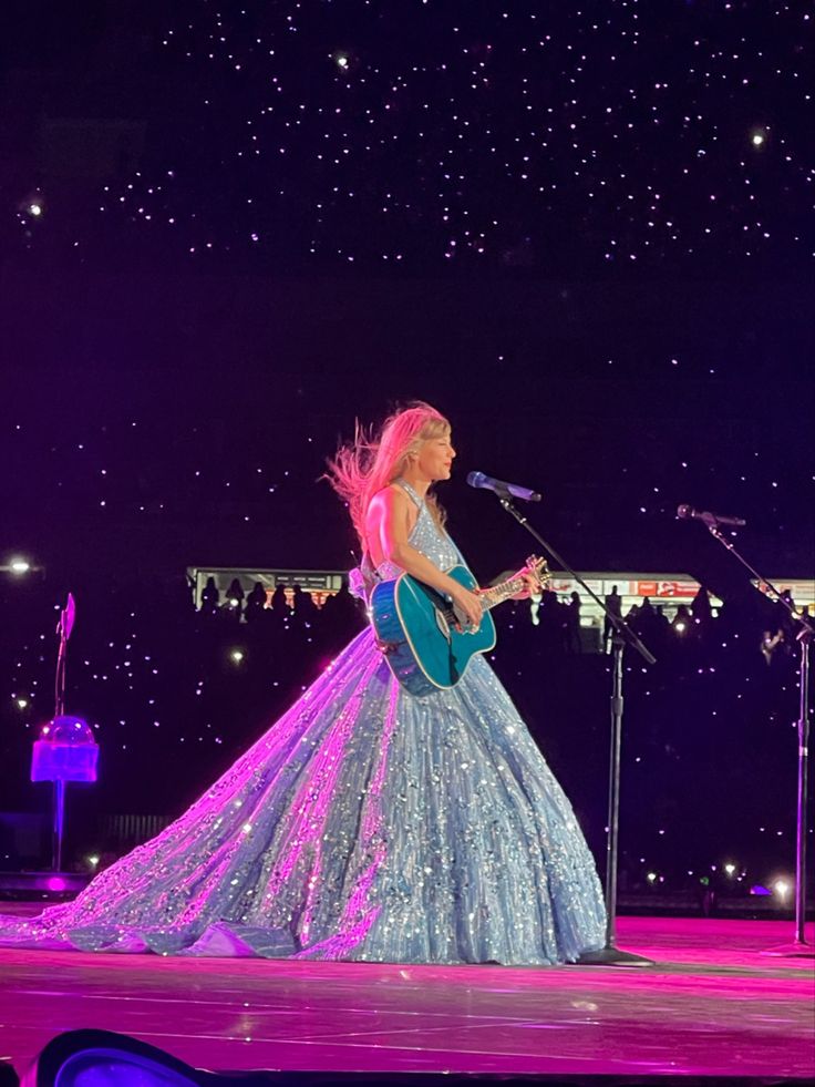 a woman in a blue dress is on stage with a guitar and singing into a microphone