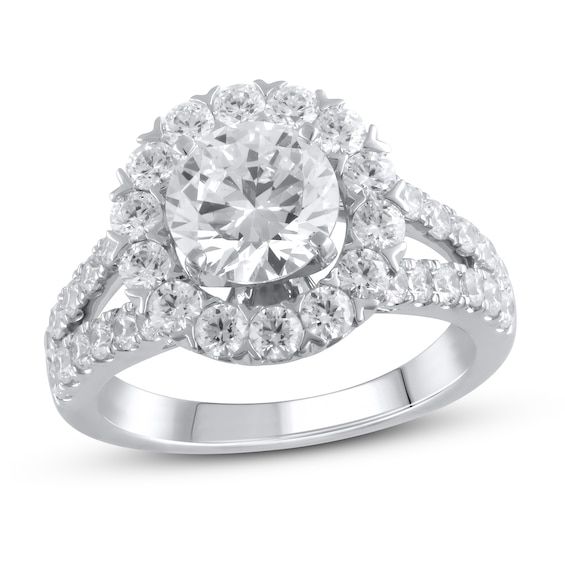 a white gold ring with an oval cut diamond surrounded by smaller round diamonds and pave set shoulders