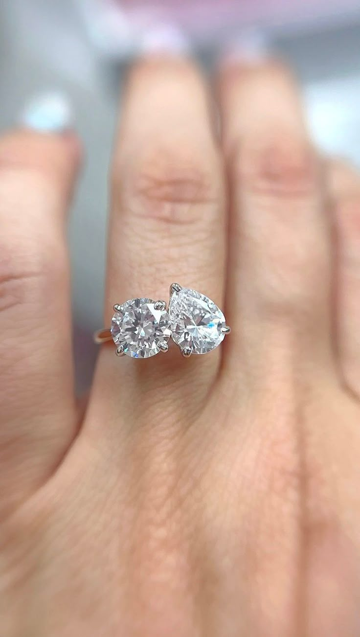 a woman's hand holding two pear shaped diamond engagement rings