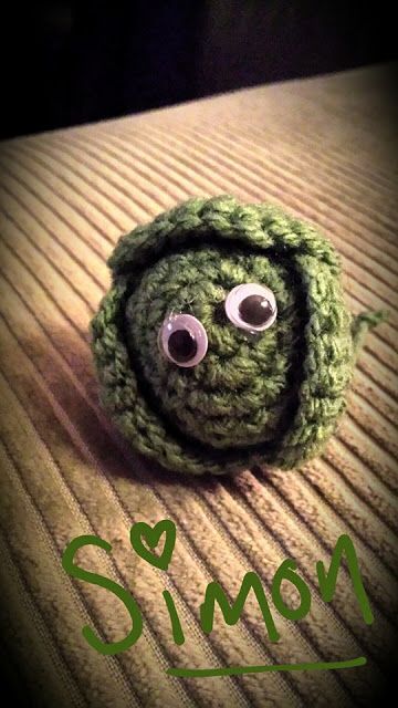 a crocheted green object with googly eyes sitting on top of a wooden table