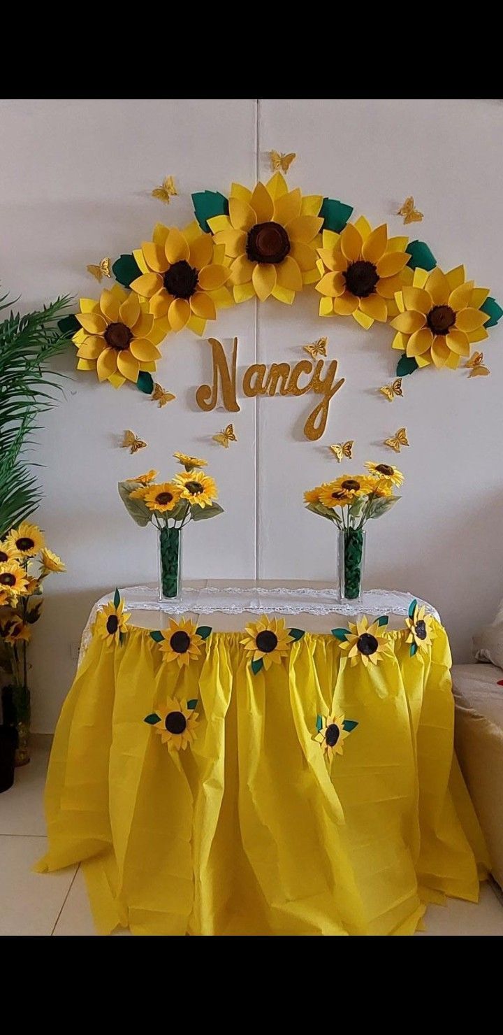 a table topped with vases filled with sunflowers next to a sign that says namcy