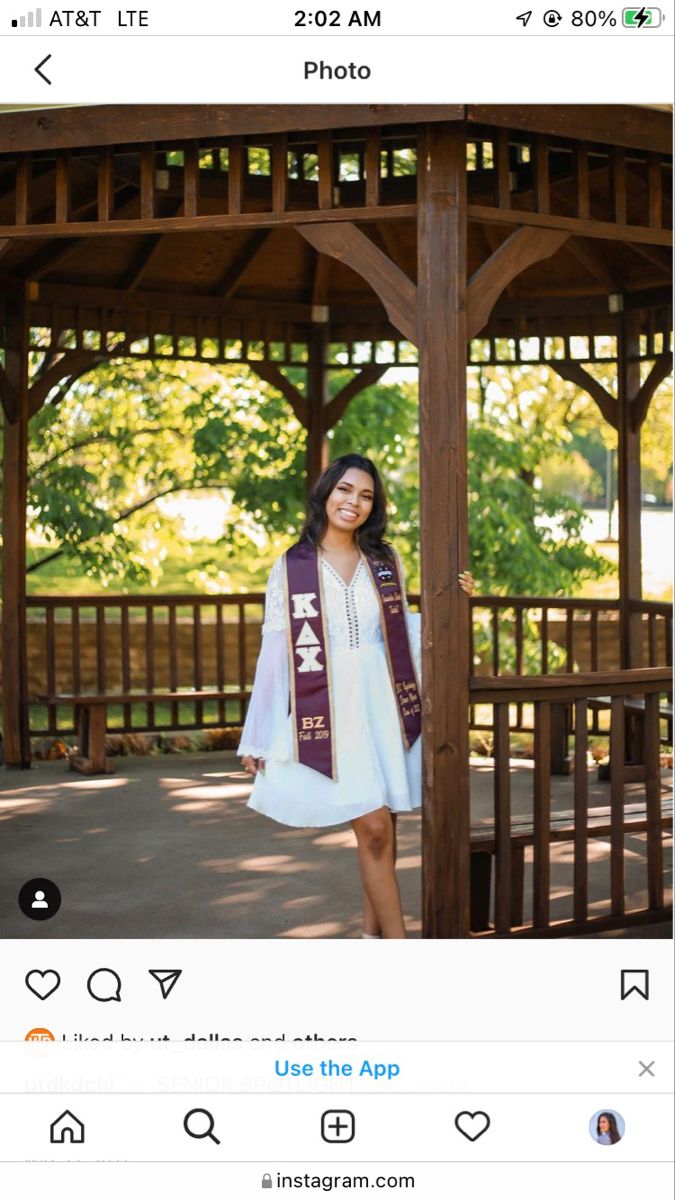 a woman standing in front of a gazebo wearing a white dress and purple scarf