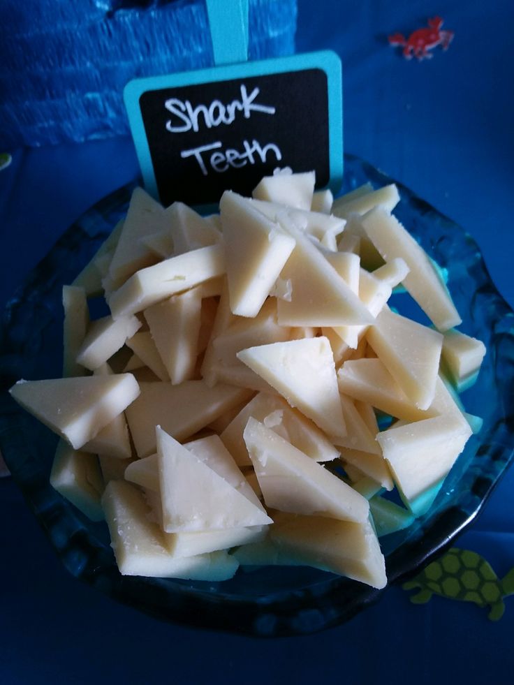 a blue plate topped with chunks of cheese next to a chalkboard that says shark teeth