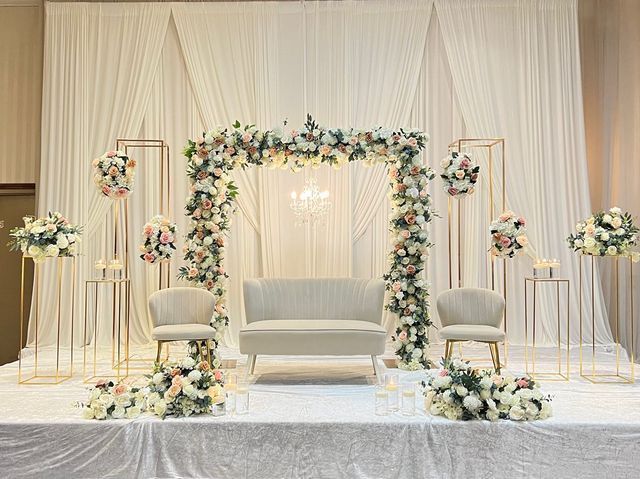 a wedding ceremony setup with white chairs and flowers on the back drop cloth draped backdrop