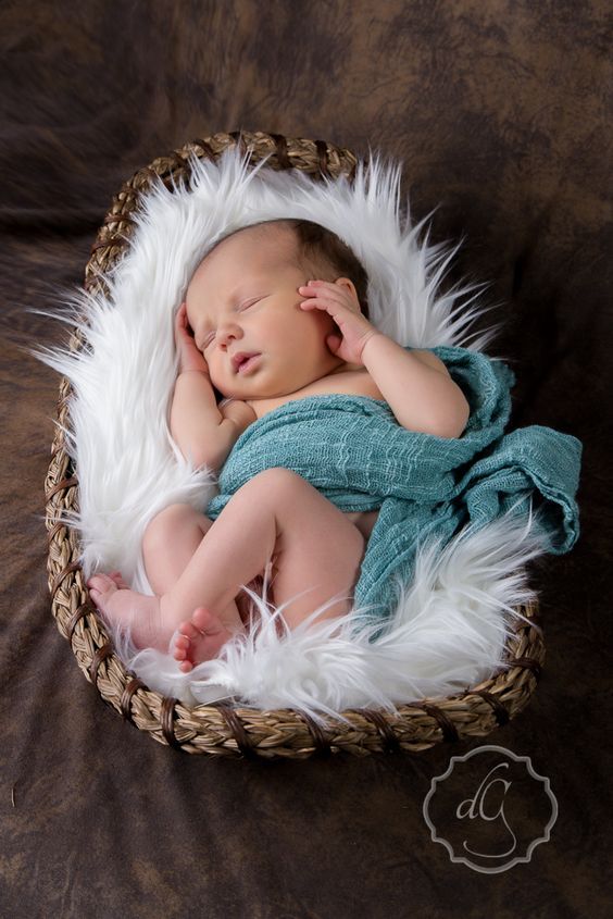 a newborn baby is sleeping in a basket with white fur on the floor and brown background