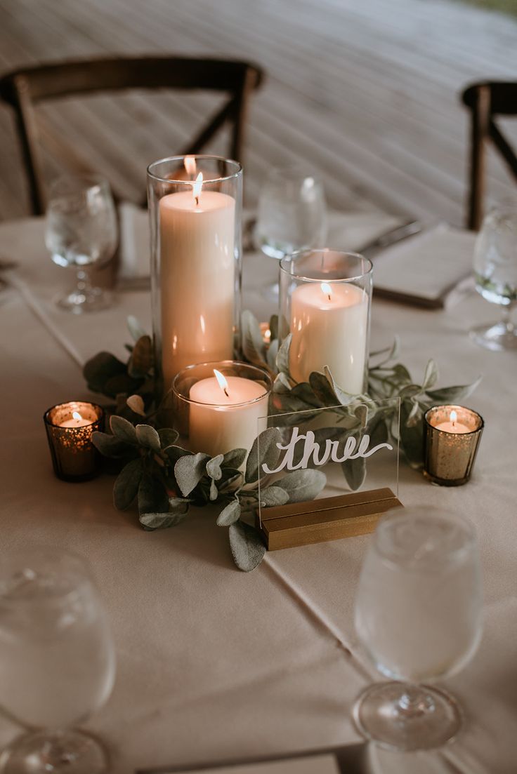 candles and greenery on a table at a wedding reception with the word true written in cursive