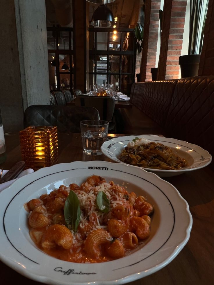 two plates filled with pasta and sauce on top of a wooden table in a restaurant