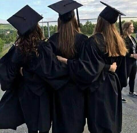 four graduates in black gowns and caps are standing together on the street with their arms around each other