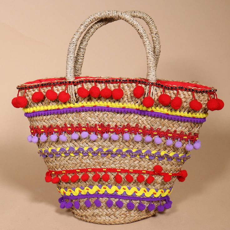 a woven basket with red, yellow, and purple pom - poms on it