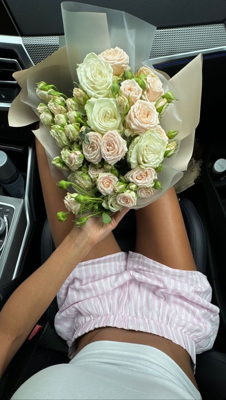 a woman laying in the back seat of a car holding a bouquet of flowers on her lap