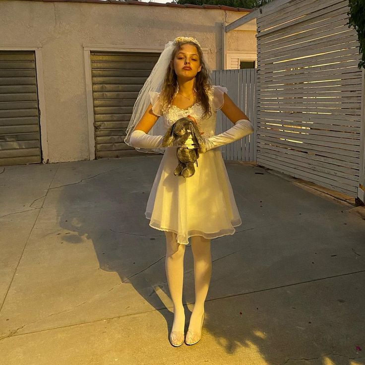 a woman in a yellow dress holding a teddy bear and wearing a white bridal veil