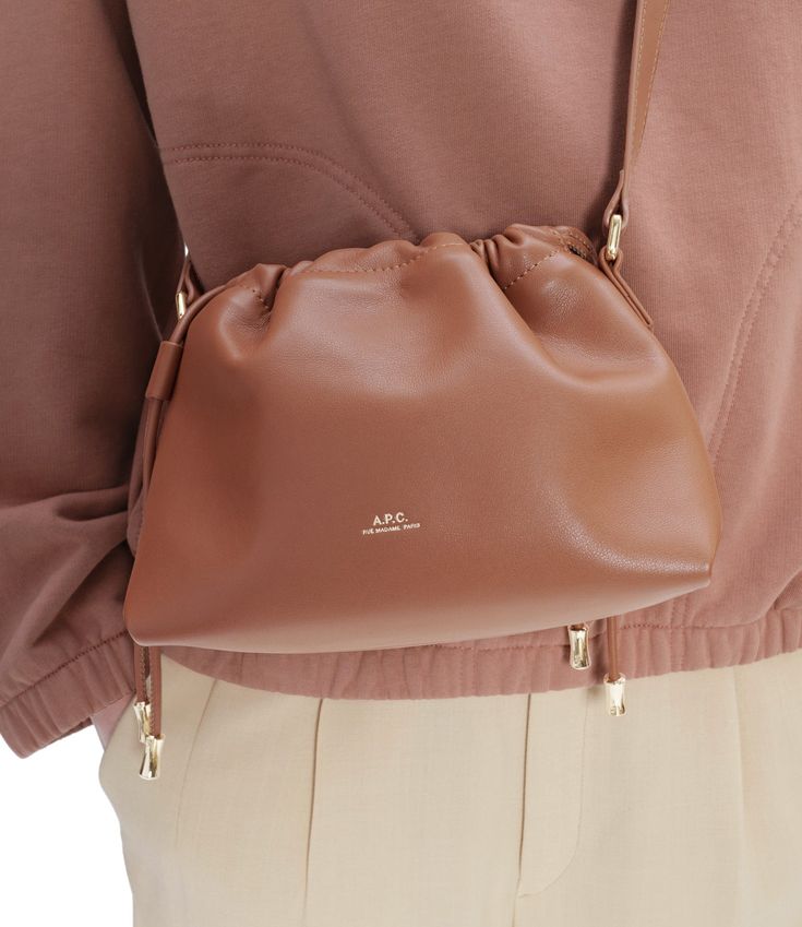 A.P.C. Women's bag. - Recycled leather-like material. - Interior magnetic closure. - Drawstring closure on top. - Strap to wear the bag on the shoulder or across the chest. - 1 interior pocket. - Goldtone 'A.P.C. Rue Madame Paris' logo embossed on front. - In the same line as the Ninon bag, Ninon Shoulder bag, Ninon drawstring bag, Ninon Small drawstring bag and Ninon tote bag. Cognac Crossbody Satchel With Dust Bag, Versatile Brown Bucket Bag For Evening, Chic Cognac Pouch Shoulder Bag, Chic Brown Shoulder Bag With Dust Bag Included, Brown Crossbody Bucket Bag For Evening, Evening Brown Crossbody Bucket Bag, Cognac Pouch Shoulder Bag For Evening, Apc Bag, Leather Drawstring Bags