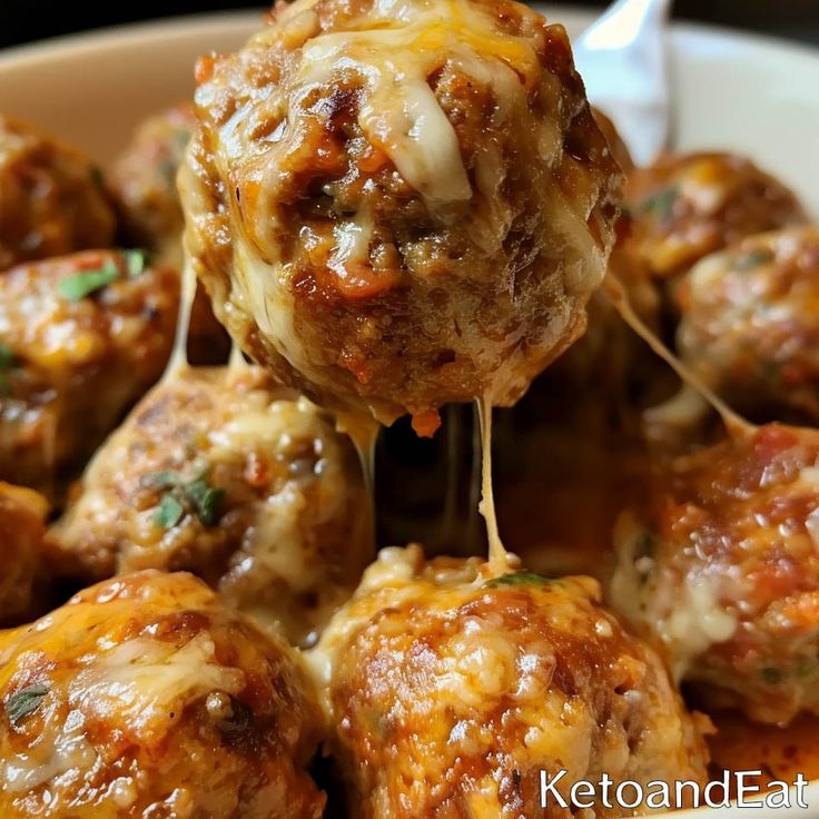 a close up of meatballs with cheese being lifted from the bowl by a fork