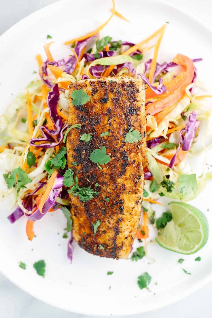 a white plate topped with fish and veggies next to a lime wedged slice