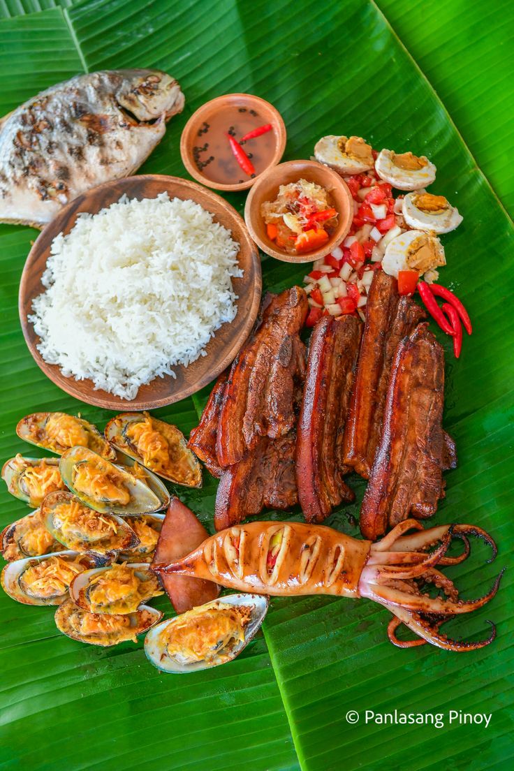 an assortment of food on a banana leaf with rice and other foods in bowls next to it