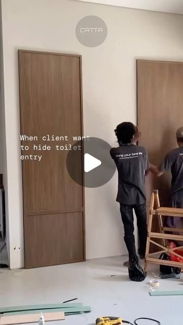 two men in black shirts are working on the wall with wood paneling behind them