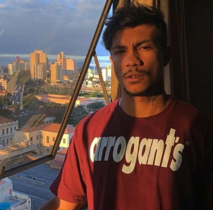 a man standing in front of a window looking out at the cityscape behind him