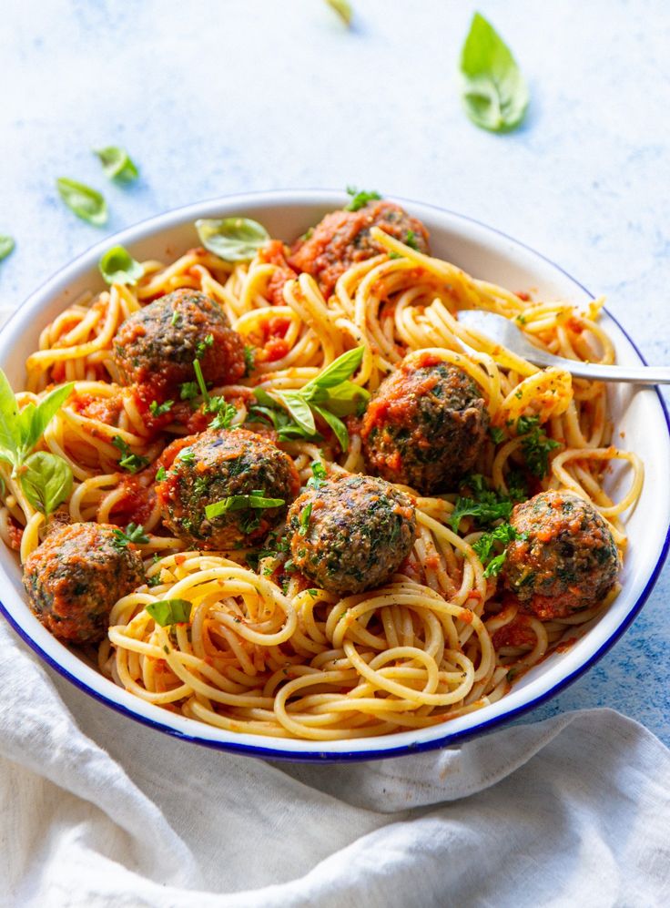 a bowl filled with spaghetti and meatballs on top of a white cloth next to a spoon