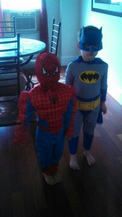 two young boys dressed up as batman and spider - man in the living room, standing next to each other