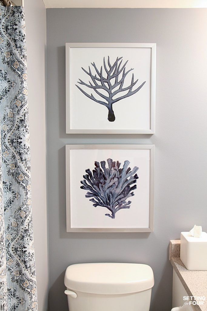 two framed pictures hang on the wall above a toilet in a bathroom with blue and white decor